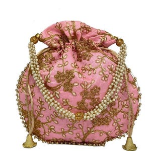 May include: A pink drawstring bag with gold floral embroidery. The bag has a pearl beaded handle and gold tassels. The bag is a soft pink colour and has a round shape.