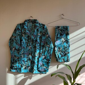 May include: A turquoise blue pajama set with a tropical print featuring palm trees and monkeys. The set includes a long-sleeved shirt and pants.