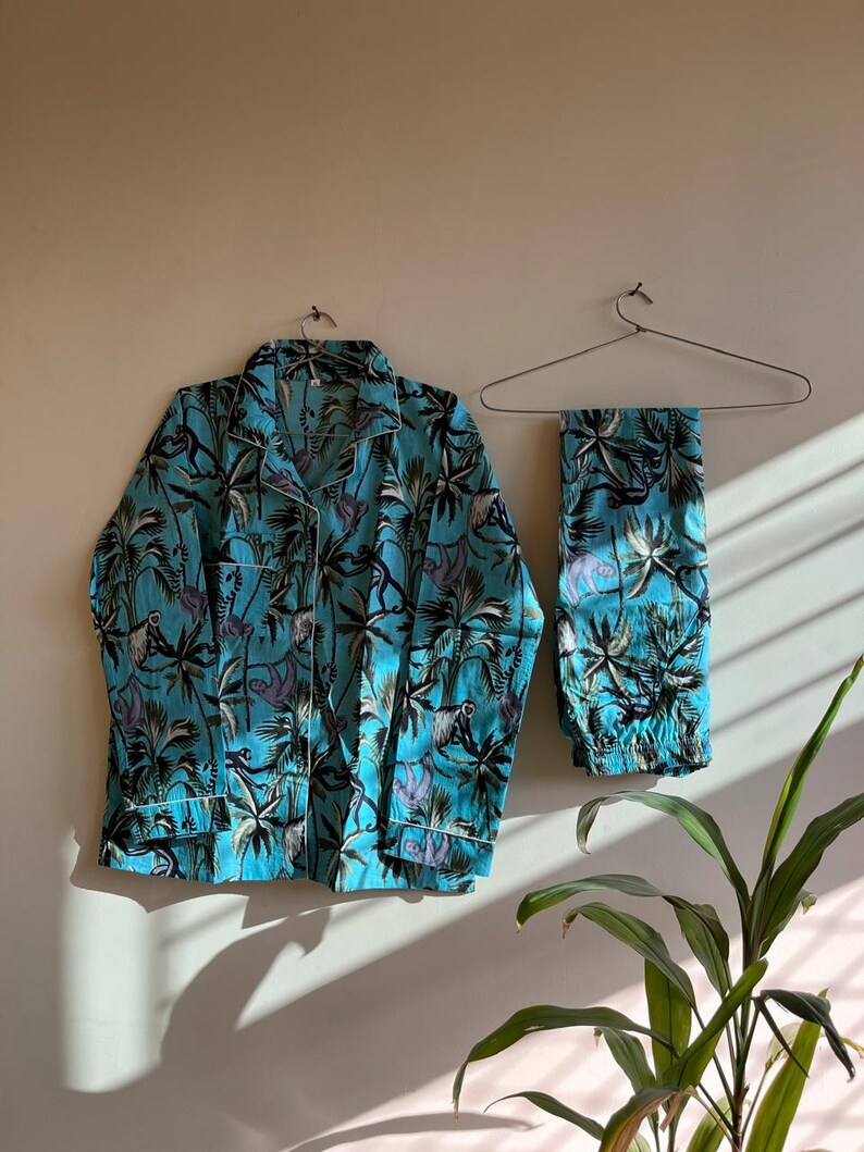 May include: A turquoise blue pajama set with a tropical print featuring palm trees and monkeys. The set includes a long-sleeved shirt and pants.