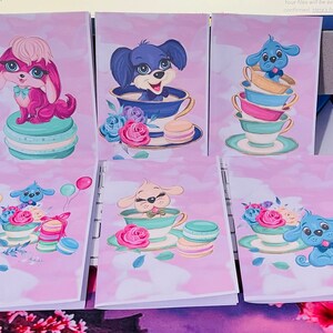Puede incluir: Un conjunto de tarjetas de felicitación con ilustraciones de cachorros de dibujos animados. Cada tarjeta presenta un diseño diferente, con colores pastel, detalles florales y macarons. Las tarjetas están sobre un fondo rosa claro y nublado.