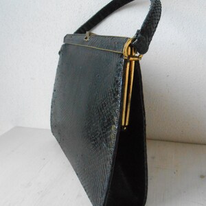 Peut inclure: Sac à main vintage noir avec un motif texturé semblable à celui d'un reptile. Le sac a une forme structurée, une poignée supérieure et des détails métalliques dorés sur le fermoir et le cadre. La poignée est tressée.