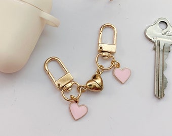 Peut inclure: Porte-clés en or avec deux breloques en forme de cœur rose et une breloque en forme de cœur dorée. Le porte-clés est attaché à une clé argentée.
