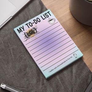 May include: A notepad with a gradient background of purple, pink, and blue, featuring the text "MY TO-DO LIST" in black. The notepad has a coffee cup illustration and the text "Where's my coffee?!" and the text "I better add procrastinate to the list."