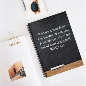 May include: A black spiral-bound notebook with white text that reads: "If no one comes from the future to stop you from doing it, then how bad of a decision can it REALLY be?" A gold paper clip and sunglasses are also visible.