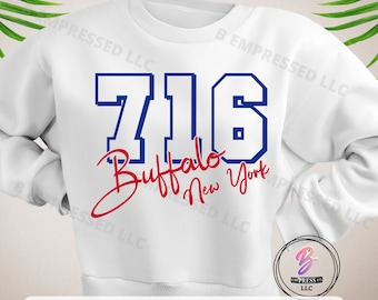 Puede incluir: Una sudadera blanca con un número "716" azul y blanco y las palabras "Buffalo New York" en escritura cursiva roja.