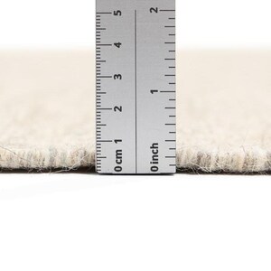 May include: Close-up of a beige rug with a ruler measuring the pile height at 1.2 cm.