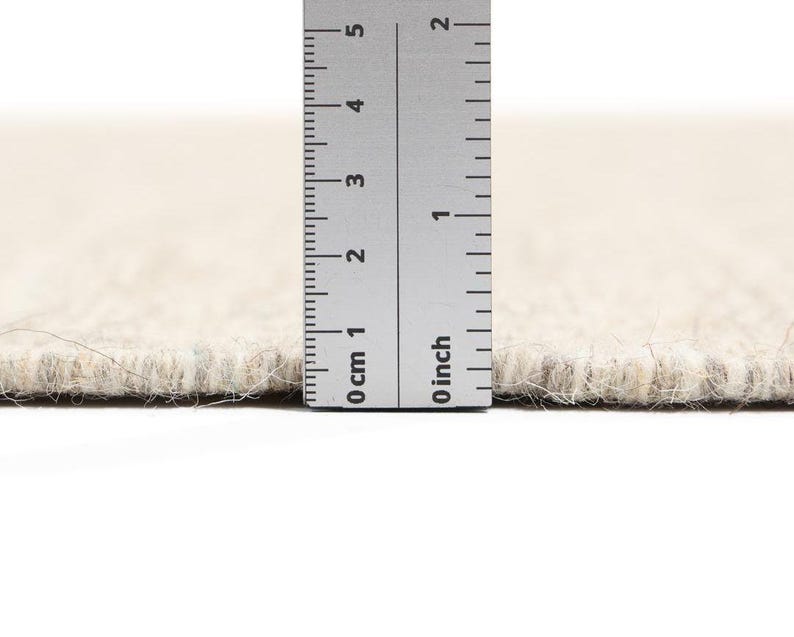 May include: Close-up of a beige rug with a ruler measuring the pile height at 1.2 cm.