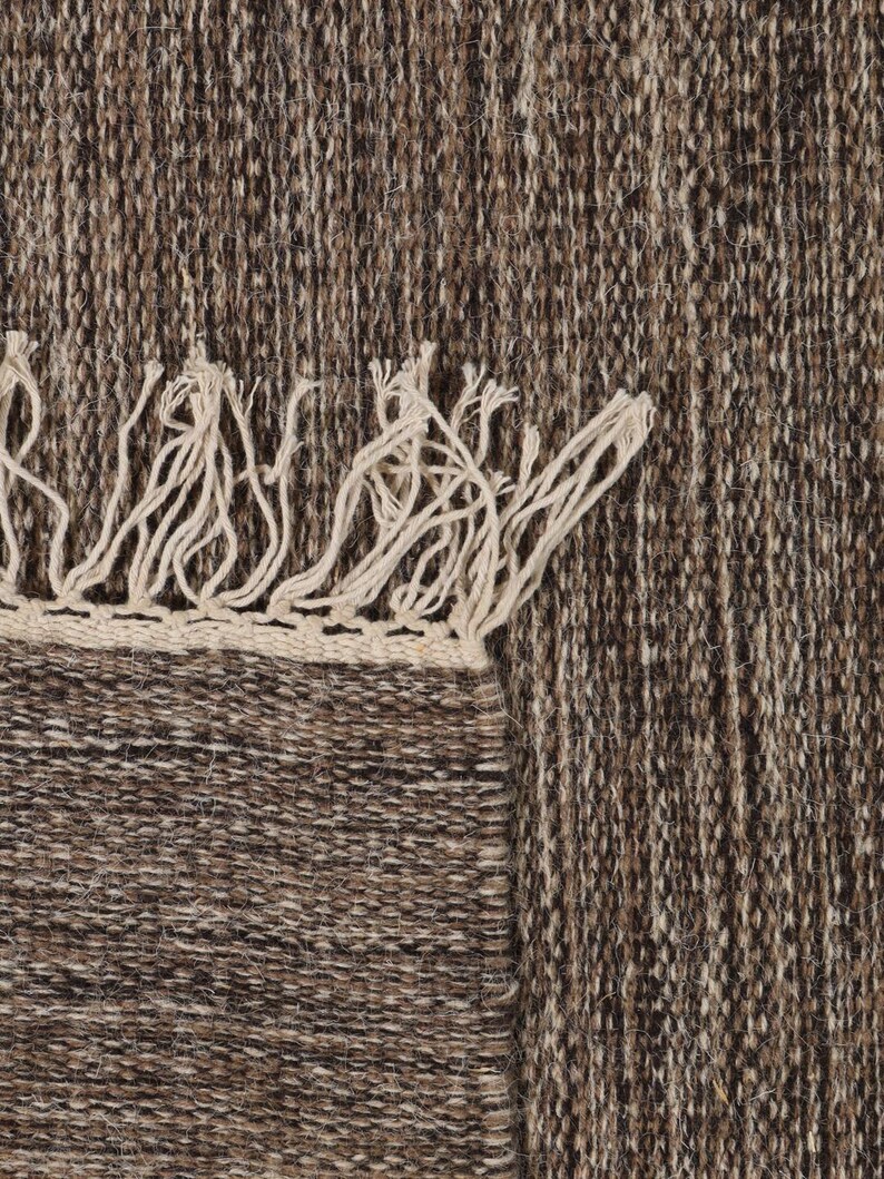 May include: A brown and beige woven rug with fringe on the edges.