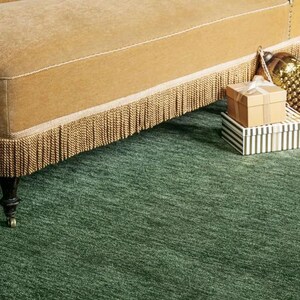 May include: A section of a gold velvet chaise lounge with a fringed trim, set on a green rug. Two gift boxes, one brown and one striped, are stacked on the rug. A gold ornament is visible.