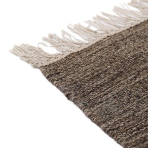 May include: A brown and beige woven rug with fringe on all sides. The rug is made of natural fibers and has a rustic look.