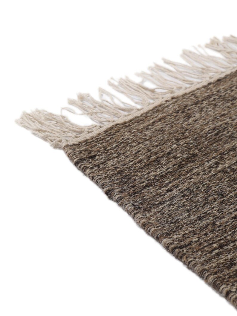 May include: A brown and beige woven rug with fringe on all sides. The rug is made of natural fibers and has a rustic look.