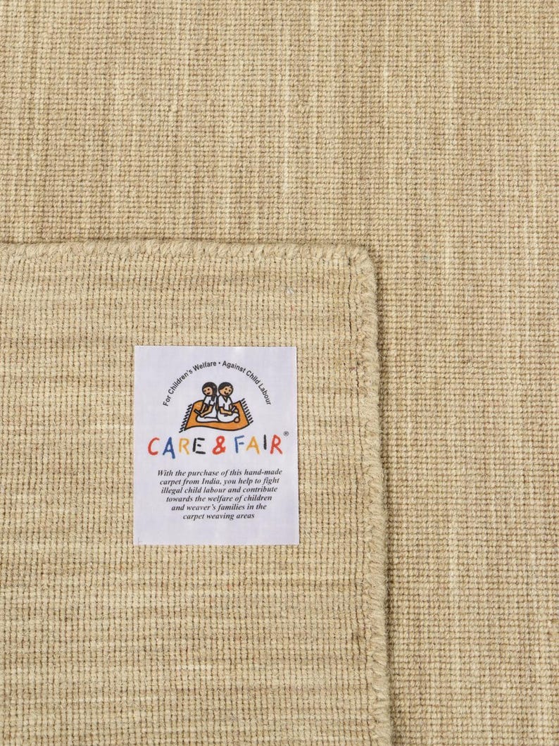 May include: A beige hand-woven rug with a label that reads "Children's Welfare Against Child Labour CARE & FAIR" and explains that the purchase of the rug helps fight illegal child labour in India.