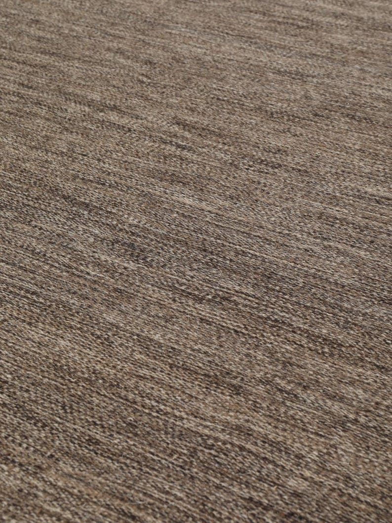May include: Close-up of a brown woven rug with a subtle texture. The rug has a natural, earthy tone and a slightly rough surface.
