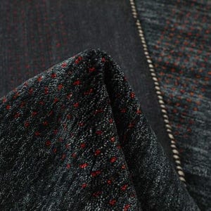 May include: Close-up of a black and gray patterned rug with red accents. The rug has a textured surface and a fringe border.