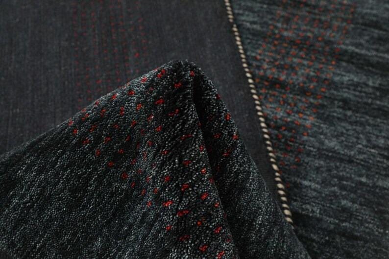 May include: Close-up of a black and gray patterned rug with red accents. The rug has a textured surface and a fringe border.