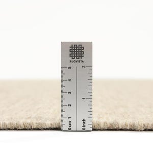 K&ouml;nnte beinhalten: Nahaufnahme eines beigen Teppichs mit einem Lineal, das 5 cm lang ist. Das Lineal tr&auml;gt den Aufdruck "RUGVISTA".