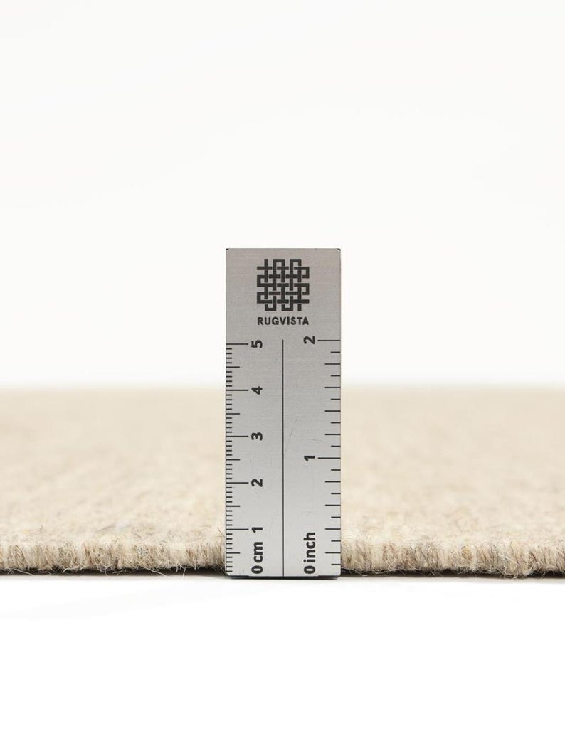 K&ouml;nnte beinhalten: Nahaufnahme eines beigen Teppichs mit einem Lineal, das 5 cm lang ist. Das Lineal tr&auml;gt den Aufdruck "RUGVISTA".