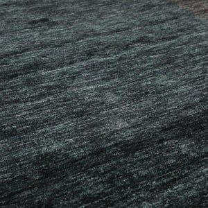 May include: Close-up of a dark gray rug with a subtle, textured weave. The rug has a slightly mottled appearance, with hints of blue and green throughout.