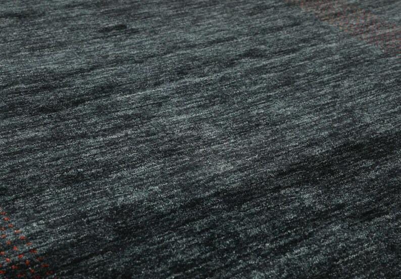 May include: Close-up of a dark gray rug with a subtle, textured weave. The rug has a slightly mottled appearance, with hints of blue and green throughout.