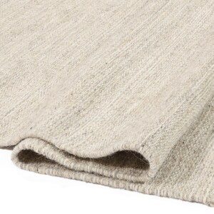 May include: A close-up of a light grey woven rug with a textured surface. The rug is folded in half, showing the edges and the weave.