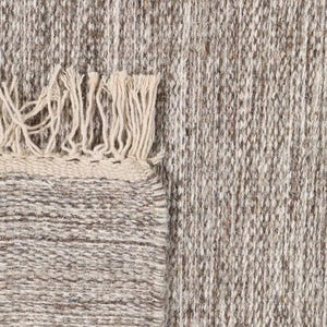 May include: A close-up of a beige and brown woven rug with a fringe border. The rug has a textured, hand-woven look.