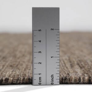 May include: Close-up of a brown and beige rug with a ruler measuring 5 cm or 2 inches.
