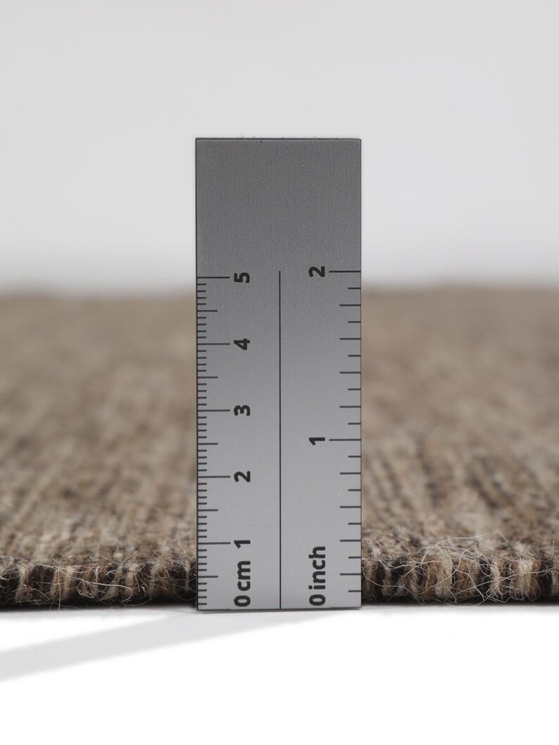 May include: Close-up of a brown and beige rug with a ruler measuring 5 cm or 2 inches.