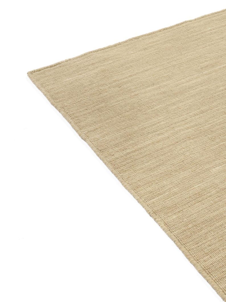 May include: A close-up of a beige woven rug with a subtle texture. The rug has a slightly rough, natural feel.