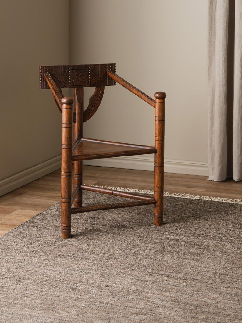 May include: A wooden chair with a carved back and intricate details. The chair has a triangular seat and legs, and is made of dark brown wood. The chair is sitting on a brown rug.