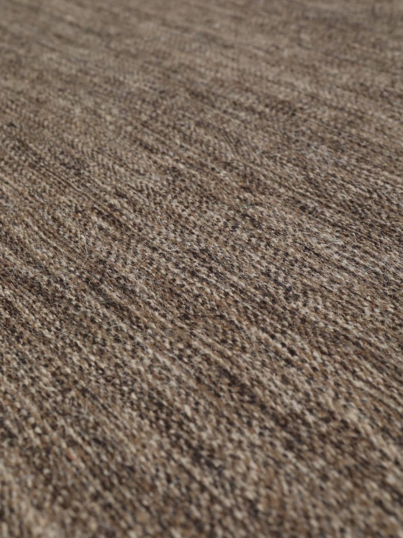 May include: Close-up of a brown and beige woven rug with a textured surface.