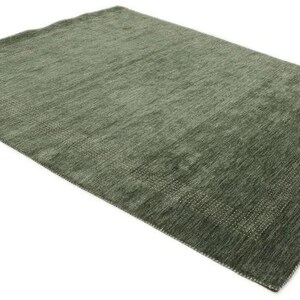 May include: A rectangular, olive green rug with a textured surface. The rug has a subtle border design and is displayed on a white background. The rug is suitable for living rooms and bedrooms.