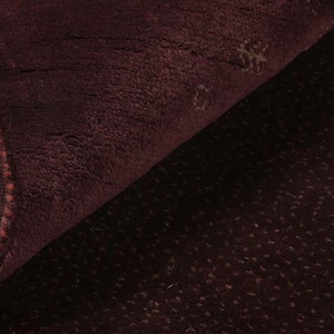 Op de afbeelding: Close-up van een donker bordeauxrood tapijt met een subtiel textuurpatroon. Het tapijt voelt zacht en pluche aan.