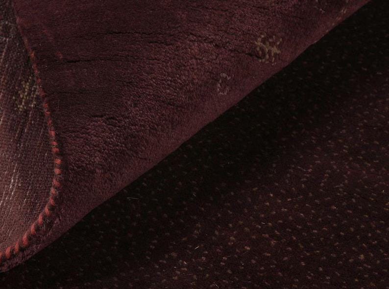 Op de afbeelding: Close-up van een donker bordeauxrood tapijt met een subtiel textuurpatroon. Het tapijt voelt zacht en pluche aan.
