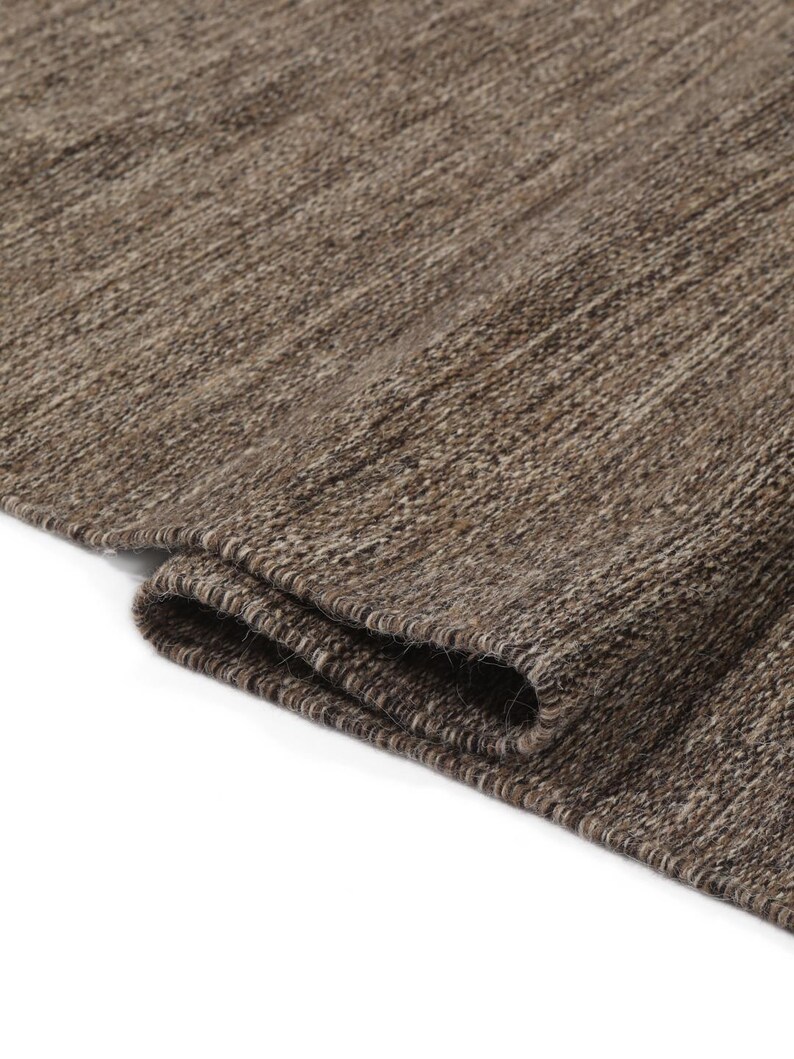 May include: Close-up of a brown and beige woven rug with a textured surface. The rug is folded in half, showing the edge of the fabric.