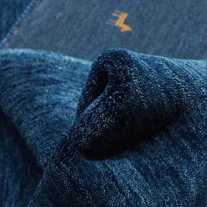 May include: Close-up of a deep blue rug with a textured, woven pattern. The rug is folded over, revealing the underside.