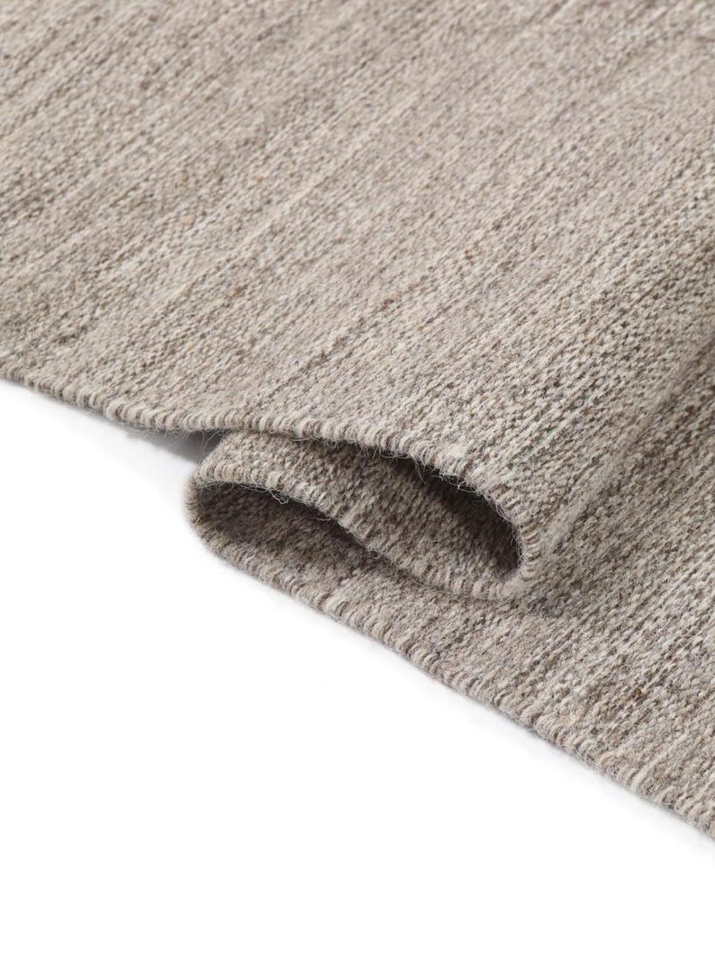 May include: Close-up of a light brown woven rug with a textured surface. The rug is folded over on itself, showing the underside of the fabric.