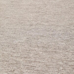 May include: A close-up of a beige rug with a textured woven pattern.