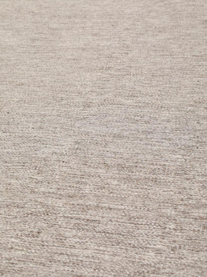 May include: A close-up of a beige rug with a textured woven pattern.