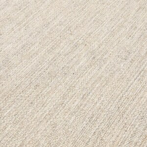 May include: A close-up of a beige woven rug with a subtle diagonal pattern. The rug has a soft, textured surface.
