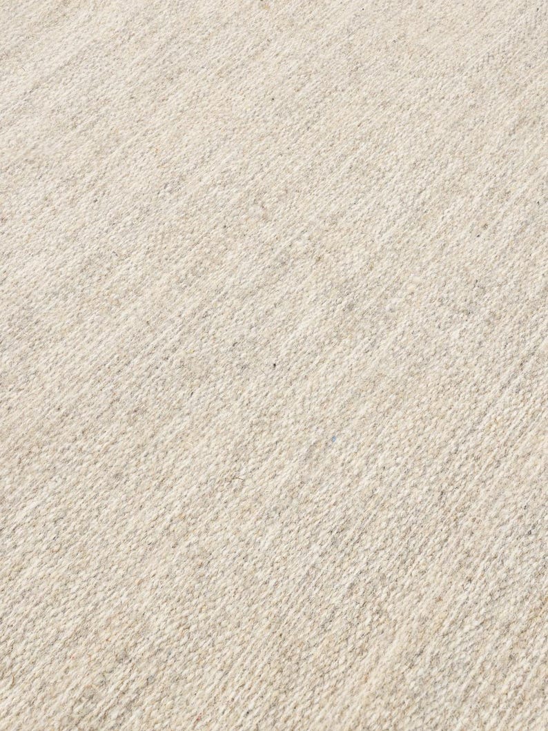 May include: A close-up of a beige woven rug with a subtle diagonal pattern. The rug has a soft, textured surface.