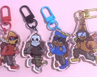 May include: Four acrylic keychains with cartoon characters, each with a different design and color scheme. The keychains have red, black, blue, and gold clasps. The characters are wearing backpacks and running. The background is a light pink.