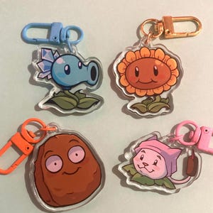 Puede incluir: Cuatro llaveros acrílicos con personajes de dibujos animados del juego Plants vs. Zombies. Los llaveros incluyen un lanzaguisantes azul, un girasol sonriente, una nuez marrón y una planta rosa con forma de gato. Cada llavero tiene un cierre de diferente color.