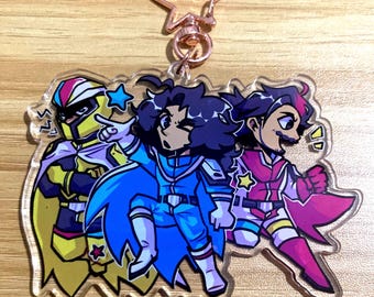 May include: A clear acrylic keychain featuring three illustrated characters in colorful superhero-style costumes. The left character wears yellow and purple, the center character wears blue, and the right character wears pink and white. A rose gold star clasp is attached.