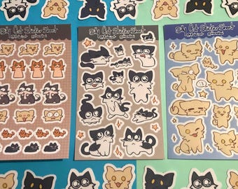 Op de afbeelding: Drie sticker vellen met katten illustraties. De vellen heten "Silly Cat Sticker Sheet" en bevatten verschillende kattenontwerpen in zwart, beige en oranje. Extra losse kattenstickers zijn verspreid.