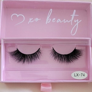 May include: A pink box with a white heart and the text "xo beauty" on the lid. The box contains two pairs of black false eyelashes. The box has a white label with the text "LX-74" on it.