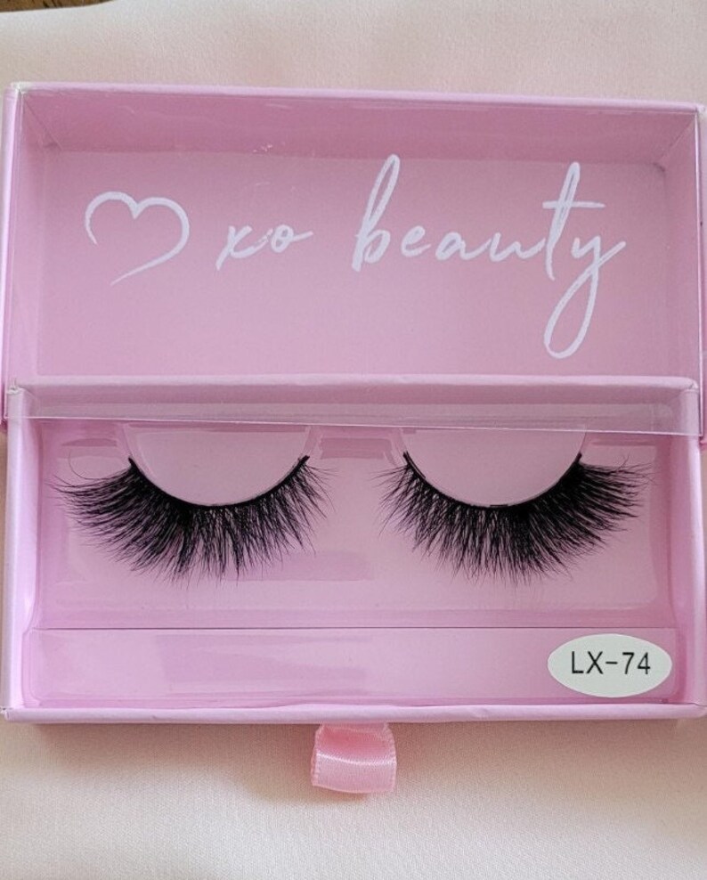 May include: A pink box with a white heart and the text "xo beauty" on the lid. The box contains two pairs of black false eyelashes. The box has a white label with the text "LX-74" on it.