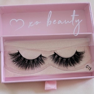 May include: A pink box with a heart and the text "xo beauty" on the top. The box contains a pair of black false eyelashes in a clear plastic container. The container has the text "G15" on the bottom right corner.