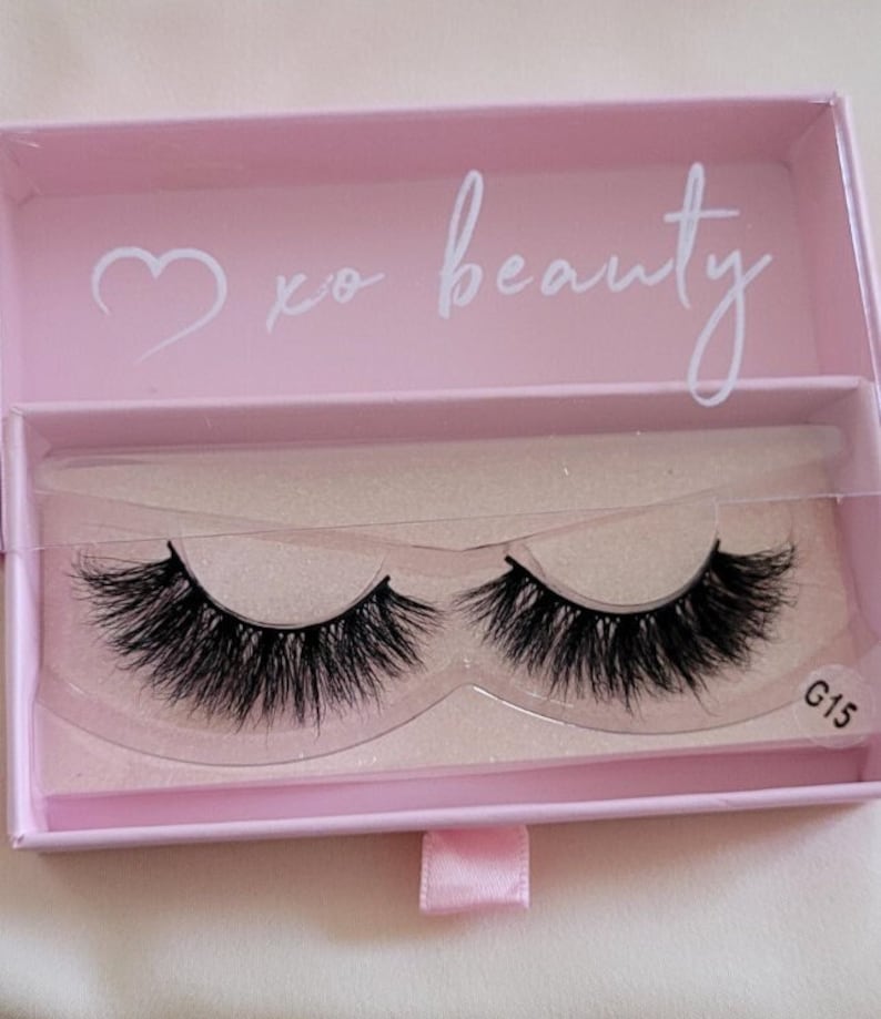 May include: A pink box with a heart and the text "xo beauty" on the top. The box contains a pair of black false eyelashes in a clear plastic container. The container has the text "G15" on the bottom right corner.