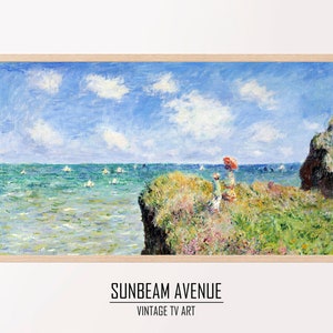 May include: A painting of a seascape with a woman in a red dress and a red umbrella standing on a cliff overlooking the ocean. The ocean is a bright blue and there are white sailboats in the distance. The sky is a light blue with white clouds. The painting is framed in a light wood frame.