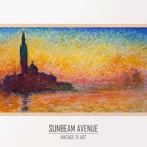 May include: A painting of a cityscape at sunset with a tall building in the center. The sky is a mix of orange, yellow, and blue. The water is a dark blue and reflects the colors of the sky. The painting is framed in a light wood frame.